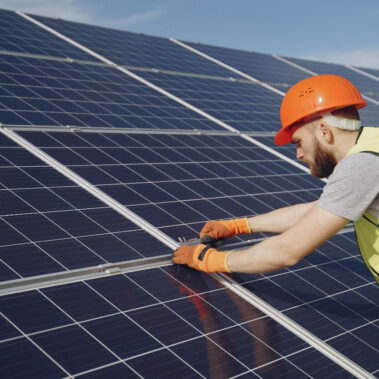 Uomo con casco e gilet catarifrangente lavora su pannelli fotovoltaici